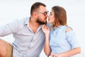 Lovely attractive couple sitting together on the white sand beach, looking each other, young couple kissing on the beach Royalty Free Stock Photo