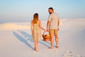 Lovely attractive couple on the white sand beach or in the desert or in the sand dunes, guy and a girl with a basket in their hand Royalty Free Stock Photo