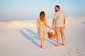 Lovely attractive couple on the white sand beach or in the desert or in the sand dunes, guy and a girl with a basket in their hand Royalty Free Stock Photo