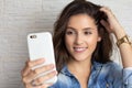 Beautiful girl is looking at cell phone screen and holding her hair. Taking a selfie, photograph. Technology, social media Royalty Free Stock Photo