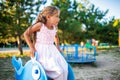 A lovely beautiful girl in a wonderful pink delicate dress sits on a small swing in a warm sunny summer park