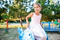 A lovely beautiful girl in a wonderful pink delicate dress sits on a small swing in a warm sunny summer park