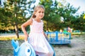 A lovely beautiful girl in a wonderful pink delicate dress sits on a small swing in a warm sunny summer park