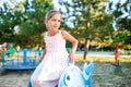 A lovely beautiful girl in a wonderful pink delicate dress sits on a small swing in a warm sunny summer park