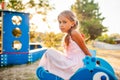 A lovely beautiful girl in a wonderful pink delicate dress sits on a small swing in a warm sunny summer park