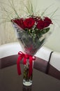 Lovely big bouquet with flowers of roses of vinous red color are standing in the glass vase on the table. Green leaves and thorns. Royalty Free Stock Photo