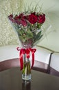 Lovely big bouquet with flowers of roses of vinous red color are standing in the glass vase on the table. Green leaves and thorns. Royalty Free Stock Photo