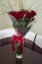 Lovely big bouquet with flowers of roses of vinous red color are standing in the glass vase on the table. Green leaves and thorns. Royalty Free Stock Photo