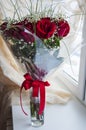 Lovely big bouquet with flowers of roses of vinous red color are standing in the glass vase on the table. Green leaves and thorns. Royalty Free Stock Photo