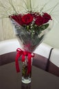 Lovely big bouquet with flowers of roses of vinous red color are standing in the glass vase on the table. Green leaves and thorns. Royalty Free Stock Photo