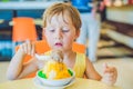 Lovely blond little boy eating ice-cream in city cafe in summer Royalty Free Stock Photo