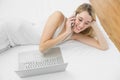 Lovely blonde woman phoning with her smartphone lying on her bed Royalty Free Stock Photo