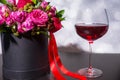 Lovely bouquet of pink and red roses and red ribbon in a circular black box near a glass with wine Royalty Free Stock Photo