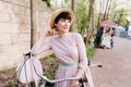 Lovely brunette woman in light-pink dress standing on street with bicycle waiting for friends. Portrait of attractive Royalty Free Stock Photo