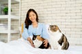 Lovely cat stand in front of Asian woman as owner with play to the other cat in bedroom and look to the left in concept of good