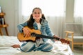 Lovely Caucacian girl enjoy to play guitar and sit on bed with day light in background and she look happy with relax activity at Royalty Free Stock Photo