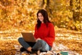 Lovely Caucasian woman using laptop for online work, browsing web at city park in autumn Royalty Free Stock Photo