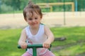 Lovely cheerful little girl kindergartner in a T-shirt rides on a swing in the park against the background of the playground