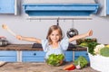 Lovely child girl joyfully raising her hands, holding wooden spoon and smiling looking at camera Royalty Free Stock Photo