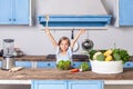 Lovely child girl joyfully raising her hands, holding wooden spoon and smiling looking at camera Royalty Free Stock Photo