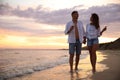 Lovely couple with glasses of wine walking on beach at sunset. Space for text Royalty Free Stock Photo