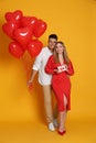 Lovely couple with heart shaped balloons and gift on yellow background. Valentine`s day celebration Royalty Free Stock Photo