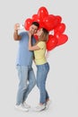 Lovely couple with heart shaped balloons taking selfie on light grey background. Valentine`s day celebration Royalty Free Stock Photo