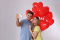 Lovely couple with heart shaped balloons taking selfie on light grey background. Valentine`s day celebration Royalty Free Stock Photo