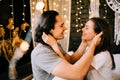 Lovely couple hugging on their bed decorated with garland lights at home indoors in the bedroom Royalty Free Stock Photo