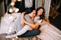 Lovely couple hugging on their bed decorated with garland lights at home indoors in the bedroom Royalty Free Stock Photo