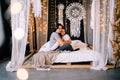 Lovely couple hugging on their bed decorated with garland lights at home indoors in the bedroom Royalty Free Stock Photo