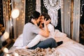 Lovely couple hugging on their bed decorated with garland lights at home indoors in the bedroom Royalty Free Stock Photo