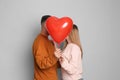 Lovely couple kissing behind heart shaped balloon on grey background. Valentine`s day celebration Royalty Free Stock Photo