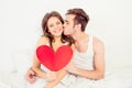 Lovely couple in love holding red paper heart in bed and kissing Royalty Free Stock Photo