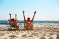 Lovely couple with Santa hats relaxing on deck chairs at beach, back view. Christmas vacation Royalty Free Stock Photo