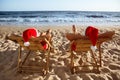 Lovely couple with Santa hats relaxing on deck chairs at beach, back view. Royalty Free Stock Photo