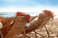 Lovely couple with Santa hats relaxing on deck chairs at beach. Christmas vacation Royalty Free Stock Photo