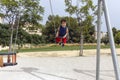 lovely curly-haired boy on swing in city park