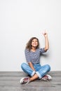 Lovely curly woman in casual clothes sitting in lotus pose on the floor being happy and candid over grey wall
