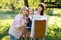 Lovely cute girl preschooler enjoying painting with her mom and grandma outdoors in beautiful summer garden on sunny day Royalty Free Stock Photo