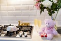 Lovely doll teddy bear with white pink roses, little present box, marshmallows and champagne on the kitchen near the stove for Royalty Free Stock Photo