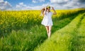 Teenage girl in white dress and Ukrainian wreath runs through yellow fields and green meadows, against cloudy sky Royalty Free Stock Photo