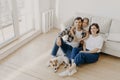 Lovely European family of father, mother and their daughter sit on floor near sofa in spacious white room, pedigree dog lies near Royalty Free Stock Photo