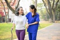 Lovely female caregiver assisting and supporting an old lady to walk with a walking stick Royalty Free Stock Photo