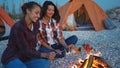 Lovely female lesbian couple sitting by campfire, prepare dinner, communicating