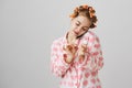 Lovely feminine caucasian blonde girl wearing hair curlers and cute nightwear with hearts, painting nails while holding