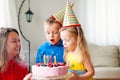 Lovely girl and boy twins in party hats blow out four candles on a birthday cake. Mom smiles Royalty Free Stock Photo