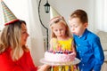 Lovely girl and boy twins in party hats blow out four candles on a birthday cake. Mom smiles and holds a cake Royalty Free Stock Photo