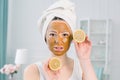 Lovely girl with brown facial mask holding a slice of lemon near her face and smiling. Photo of girl receiving spa