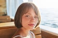 Lovely girl with dark eyes and freckles, dressed in summer dress, looking at camera while sitting at wooden bench of ship, admirin Royalty Free Stock Photo